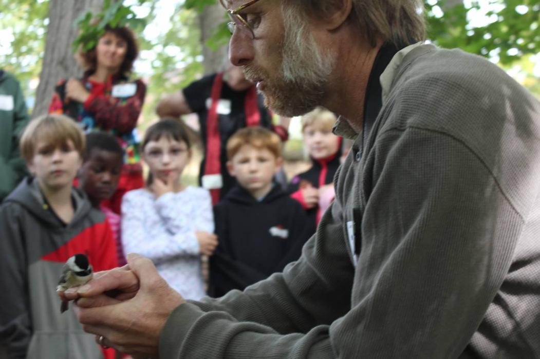 SMBC researcher Bob Reitsma holds a small bird and talks to a group of students and teachers about the Neighborhood Nestwatch program