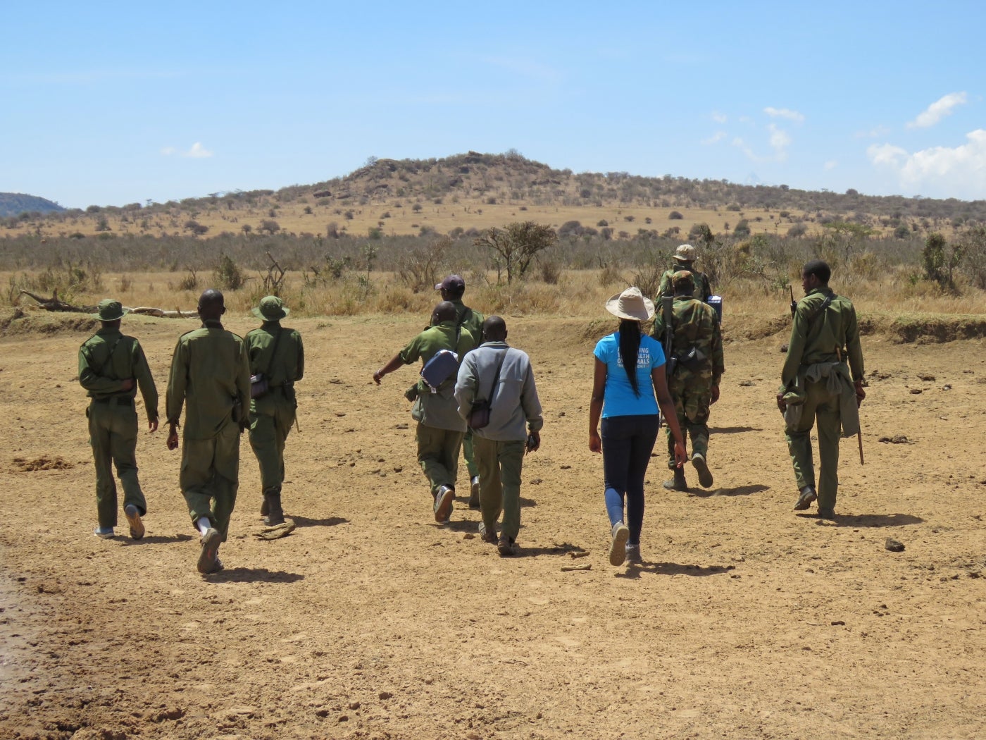 Veterinary research fellow Dr. Maureen Wanjiku Kamau and conservation manager Jamie Gaymer walk with a group of rangers at Ol Jogi Wildlife Conservancy in Kenya searching for rhino dung samples