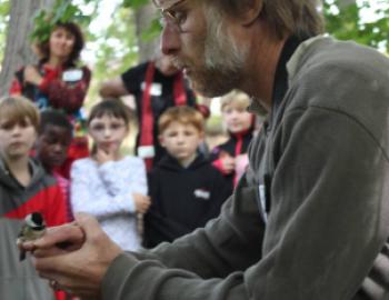 SMBC researcher Bob Reitsma holds a small bird and talks to a group of students and teachers about the Neighborhood Nestwatch program