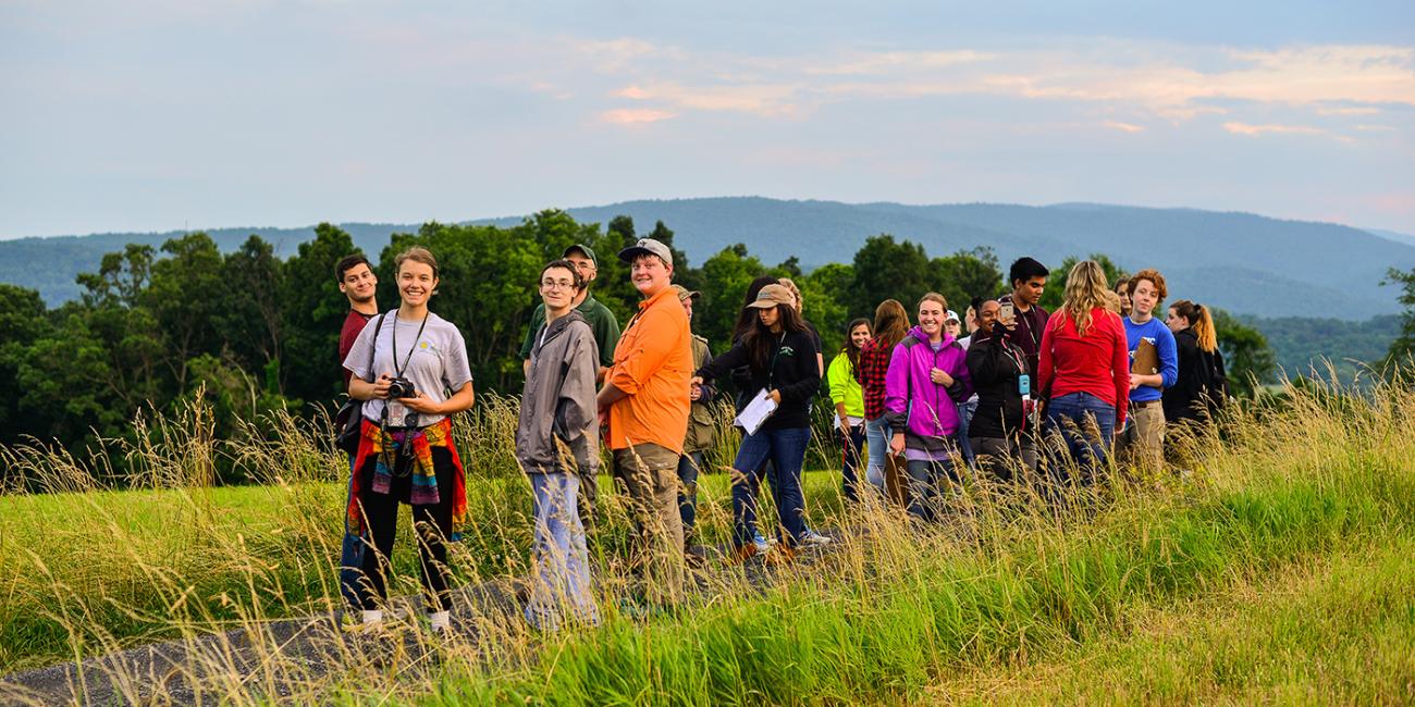 A group of students standing on a grassy mountaintop that overlooks trees and a skyline