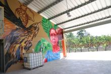 Mural by artist Evaristo Angurria at Zorzal Cacao's Central Fermentary at Zorzal Cacao in San Francisco de Macoris, Cibao, Dominican Republic. Photo: Kristen Reed Colorful mural featuring brown spotted bird and woman along with cacao pods and green leaves.