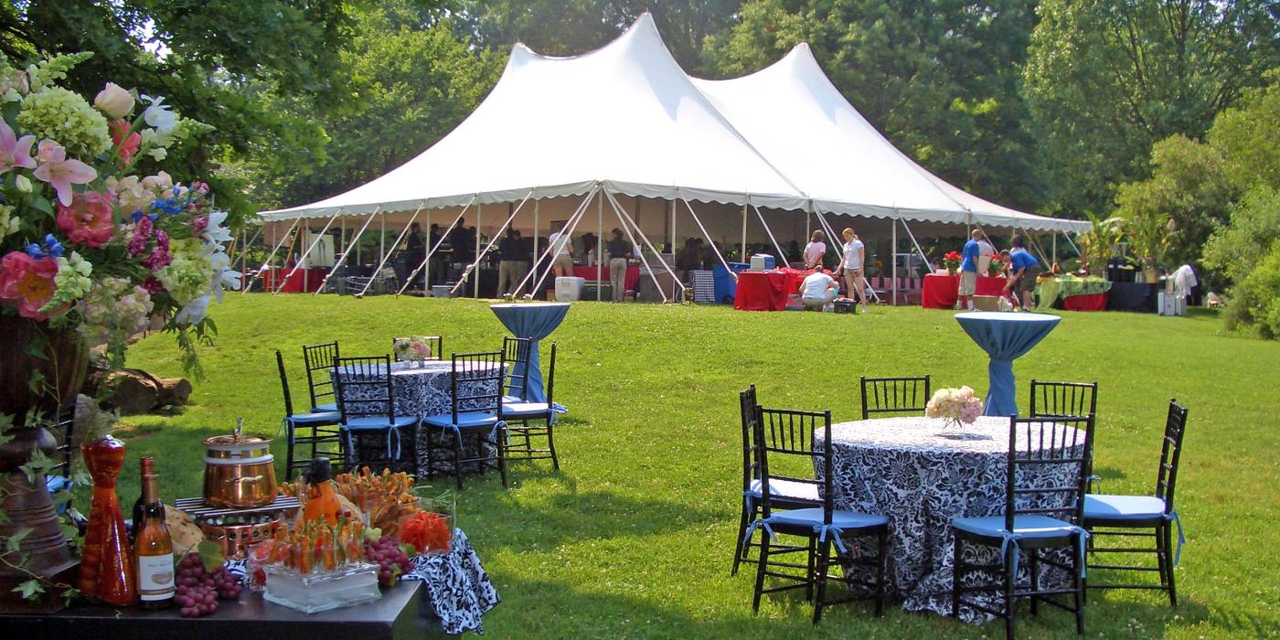 An event tent, tables and chairs set up in a grassy green meadow surrounded by trees on a sunny day at the Smithsonian's National Zoo